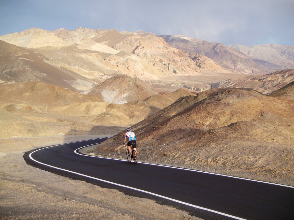 A lone cyclist on a paved trail through rolling, rocky hillsides.