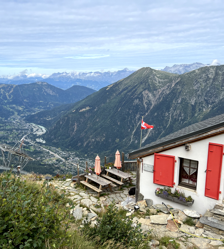 A view of the mountainous landscape with a small white building with red shutters in the foreground.