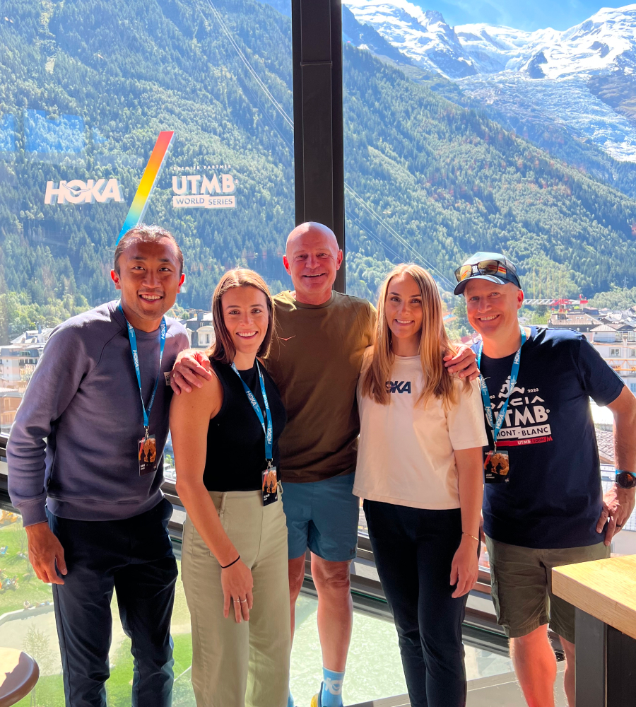 Five people face the camera smiling, standing in front of a mountain view.