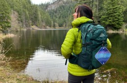 Woman stands near a lake with a pack on her back and a pee cloth dangling from it.