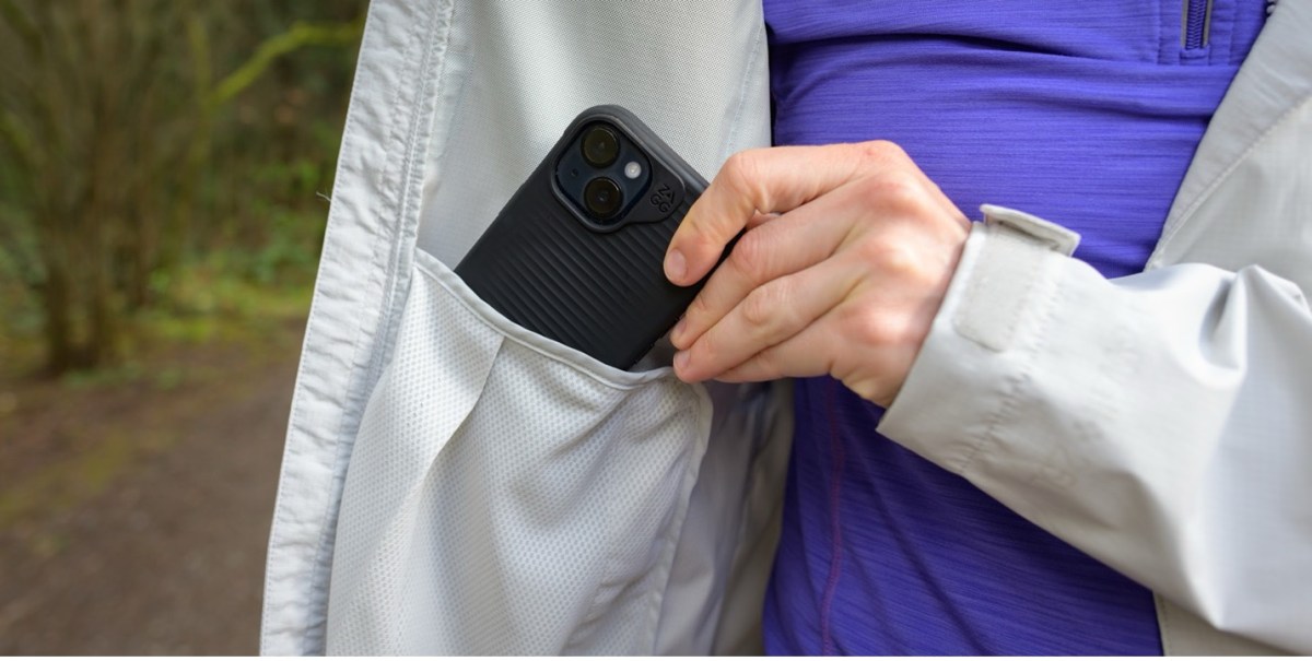 Detail of the interior drop-in pockets on the Rainier rain jacket. The model is placing an iPhone in a black case into the pocket. 