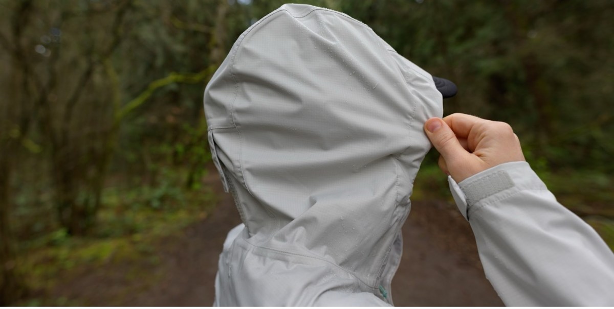 Detail of the Rainier rain jacket's adjustable hood, with adjustment bungees that are hidden inside the collar for a cleaner look. The rain jacket is a silver color.