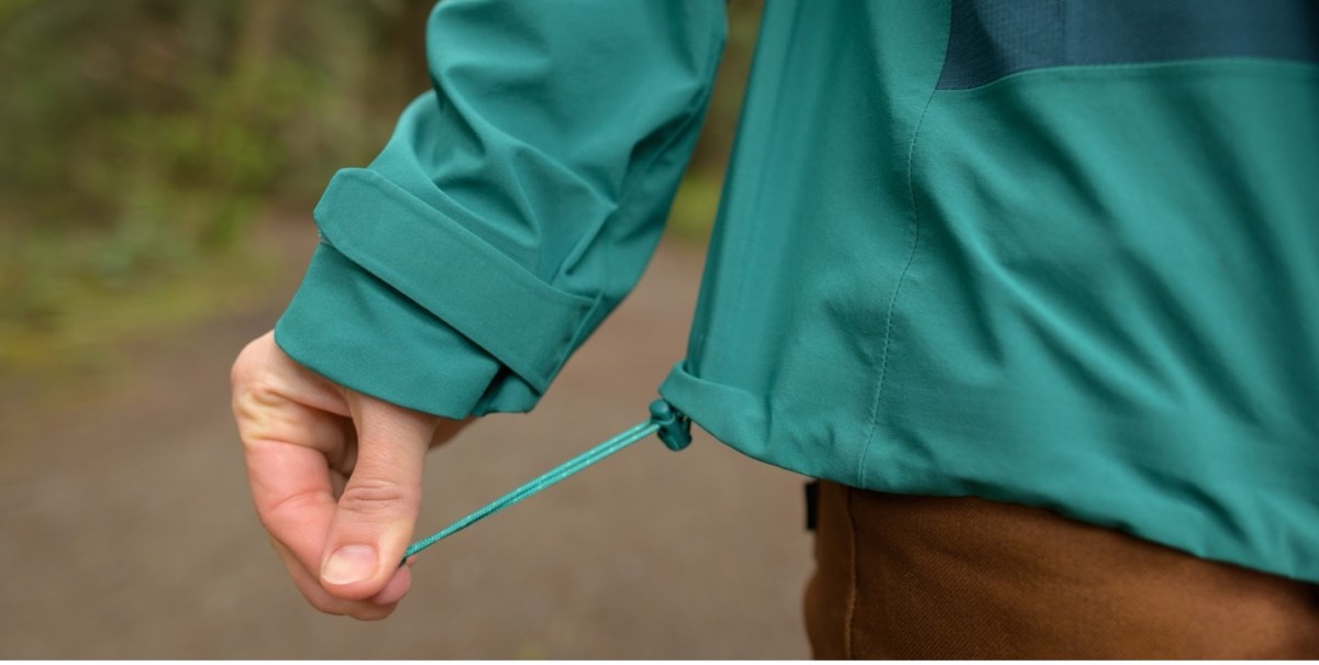 Detail of the Flash Stretch rain jacket's adjustable hem. The model pulls the drawstring that adjusts the hem away from the jacket. 