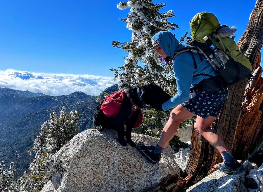 Lyla Harrod wears a blue fleece while petting a dog on a rocky outcrop.