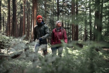 Two hikers in a forest look up at the sky