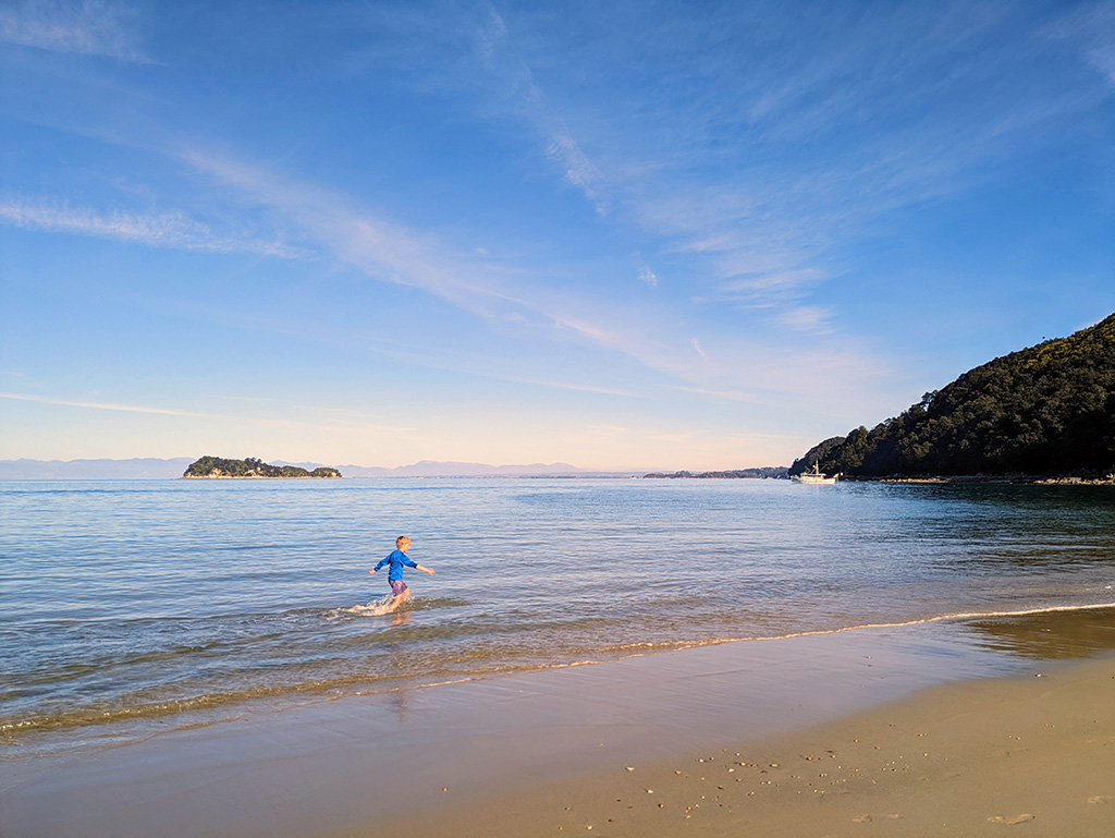 A young person runs into the shallow water along an ocean beach.