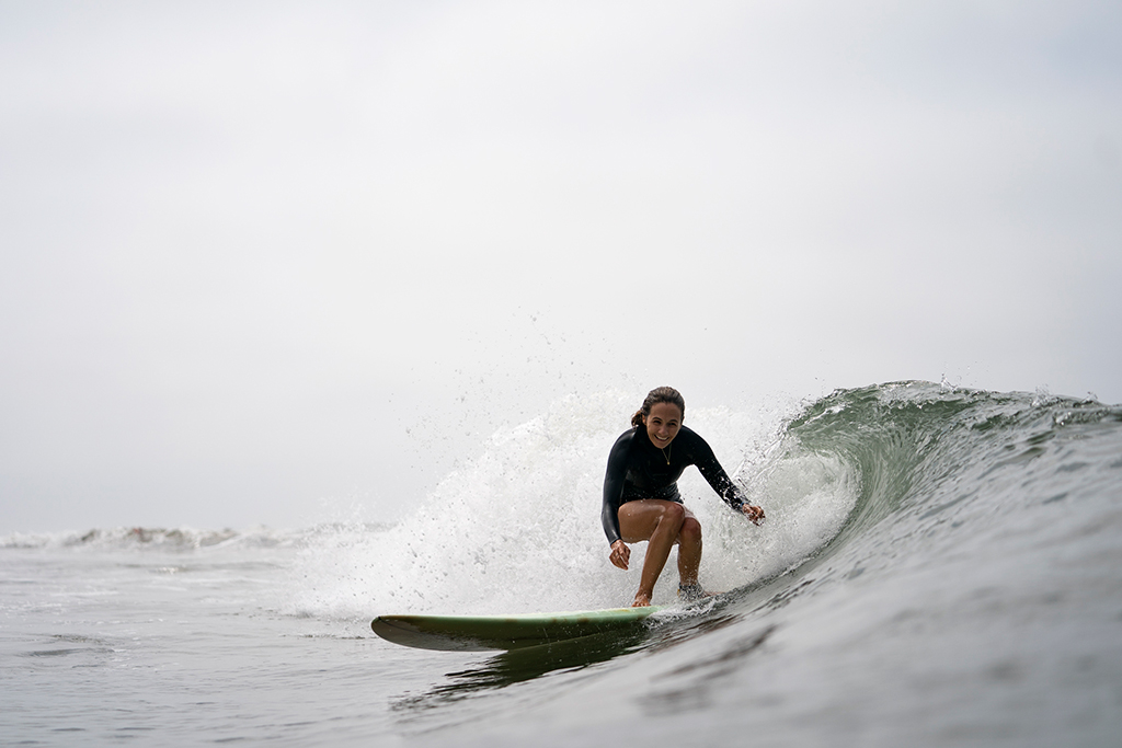 A person on a surfboard catching a wave smiles at the camera.