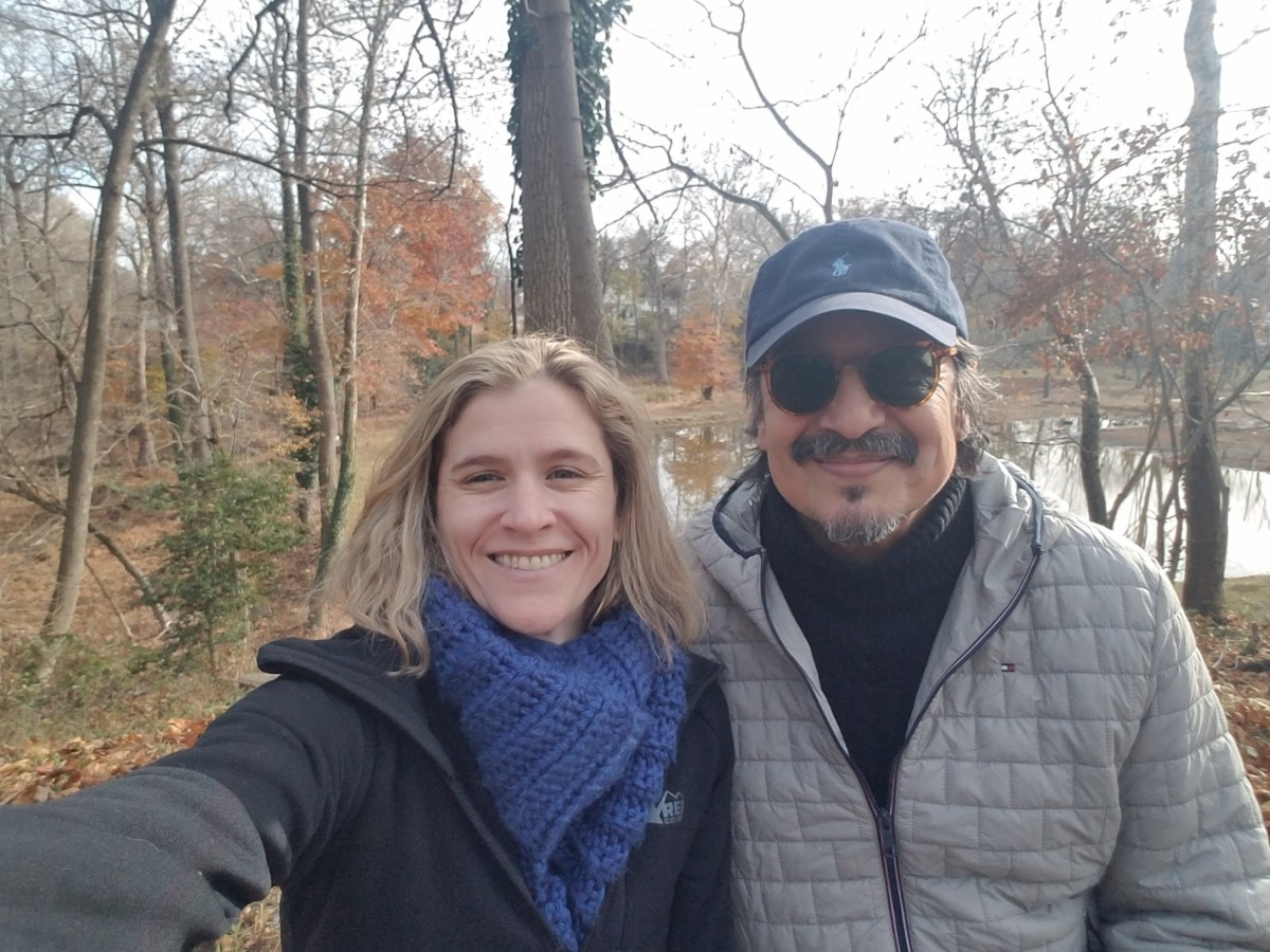 Two people smiling at the camera, standing in front of a wooded area. for their #OptOutside tradition of visiting a local park