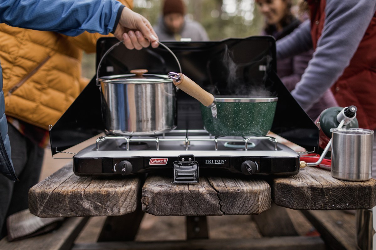 Close-up image of several people cooking over a camp stove
