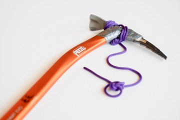 A close-up of an ice axe with an orange handle on a white background