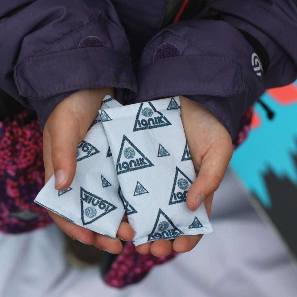 Two hands holding disposable hand warmers.