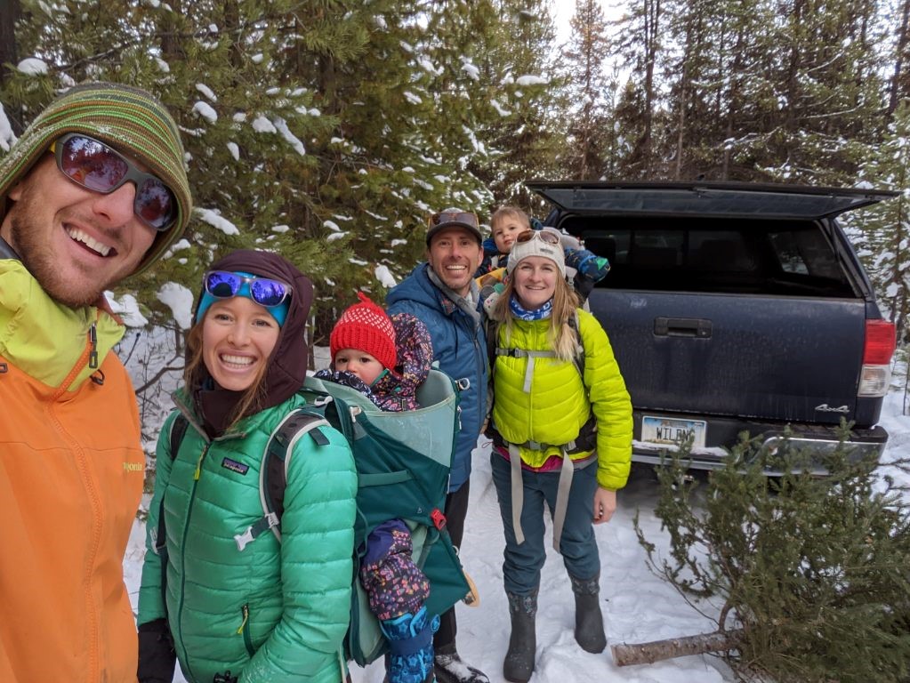 Picture of two couples posing in the snow with their small children for their #OptOutside tradition of cutting down a tree