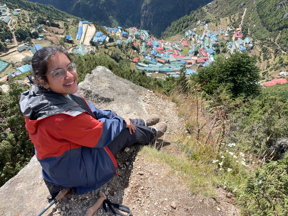 Image of woman sitting atop a rock ledge overlooking a small village.