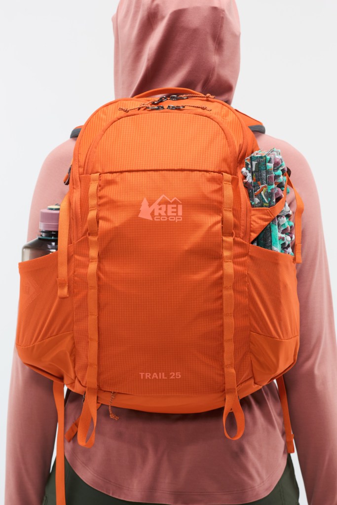 A person wearing an REI Co-op Trail 25 pack with their back and pack to the camera. Some of the pockets are full.