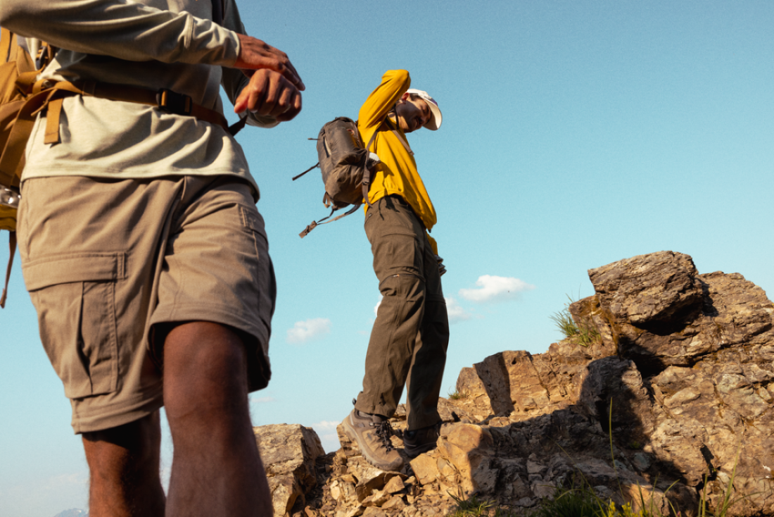 Two people stand at the top of a rocky outcropping.