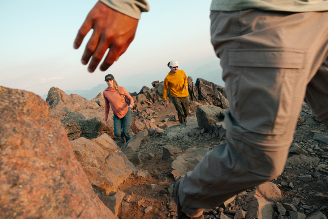 Three people are hiking; one is passing close to the camera and is only seen in partial view