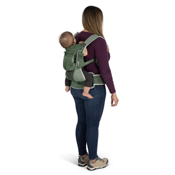 A person is wearing a soft child carrier with the child in the rear position, facing inward