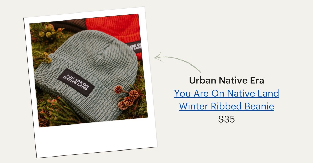 A grey beanie with the words "You Are on Native Land" in the front resting on foliage. Urban Native Era's You Are On Native Land Winter Ribbed Beanie, $35.