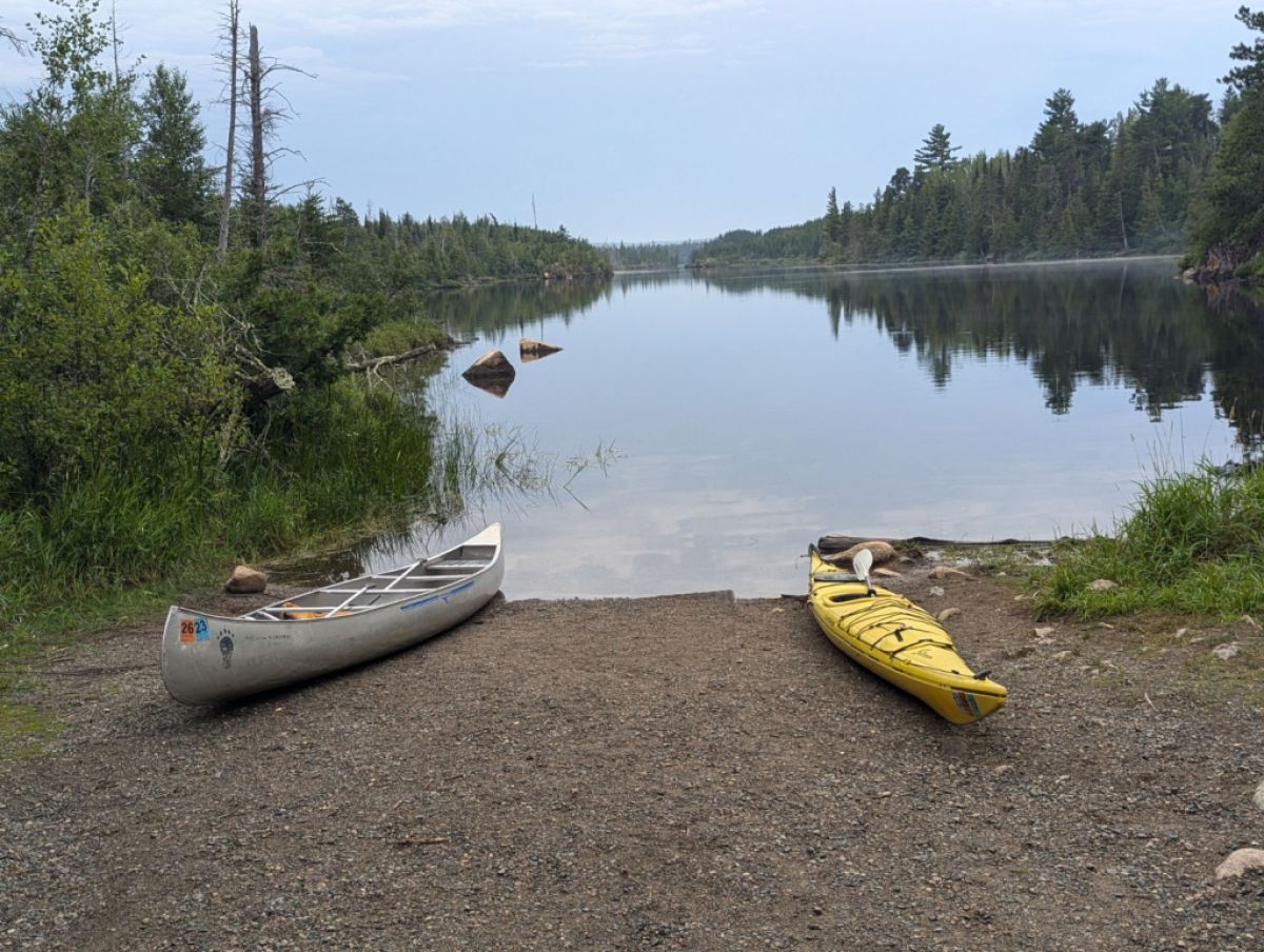 Two kayaks on the shore by a still lake.
