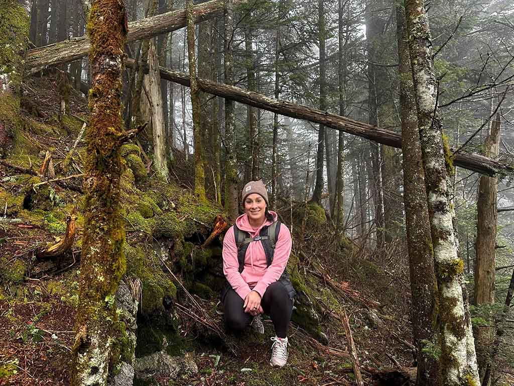 A person sitting in a mossy wood, wearing a bright pink top.