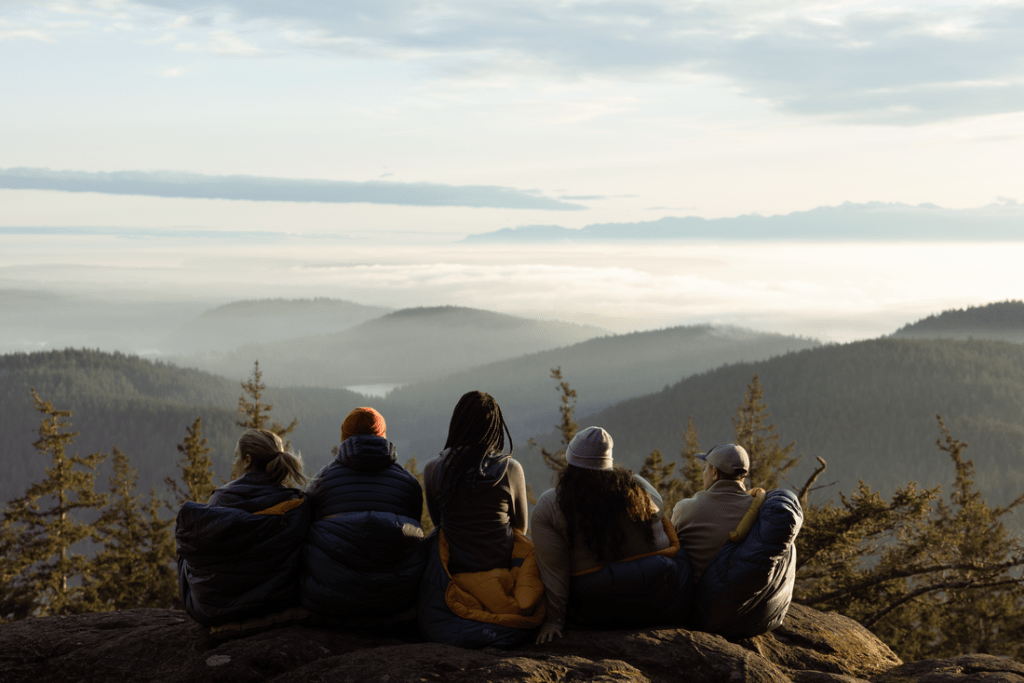 Five people with their backs turned, sitting on an overlook and gazing off at the distant hills