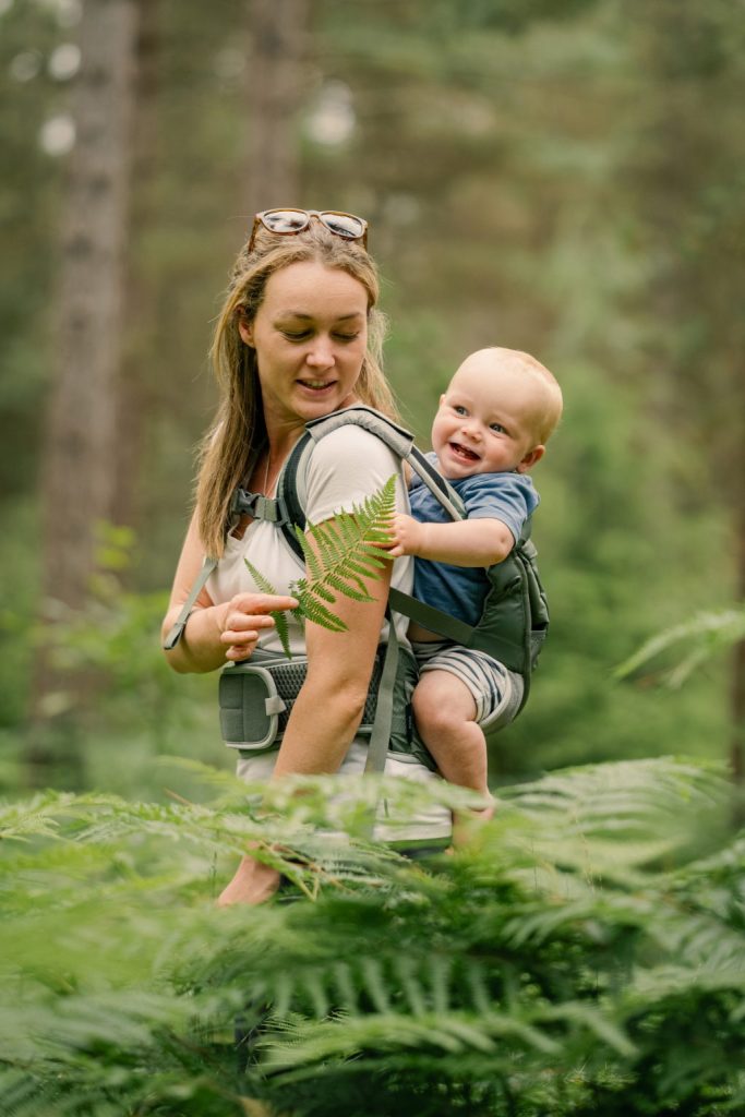 A person wears an Osprey soft child carrier with the child in the back, facing forward