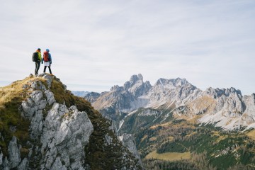 Two people hold hands atop a mountain summit.