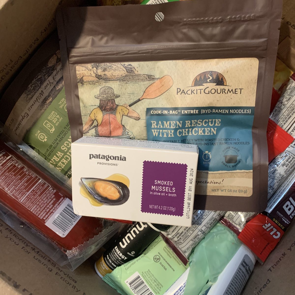 The picture shows a box of the writer's food, including smoked mussels from Patagonia Provisions and dehydrated ramen with chicken.