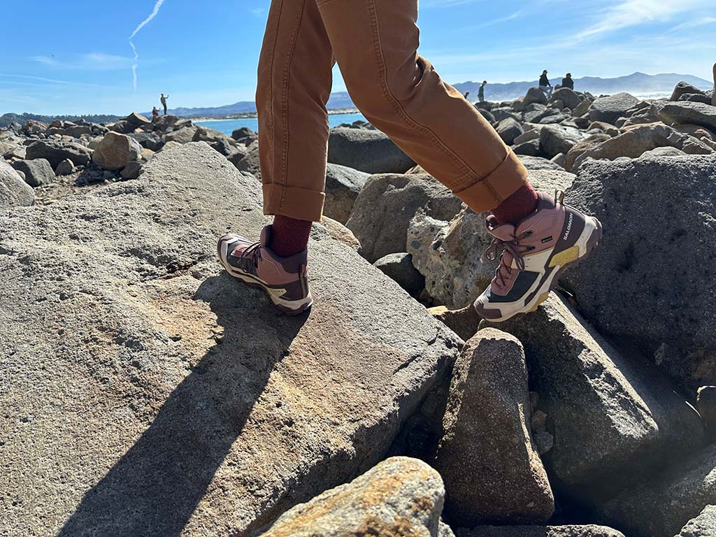 A person shown from the thighs down, crossing over rocks in hiking pants with Salomon hiking boots.