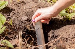 A hand displays a trowel in a cathole, demonstrating the 6" depth.