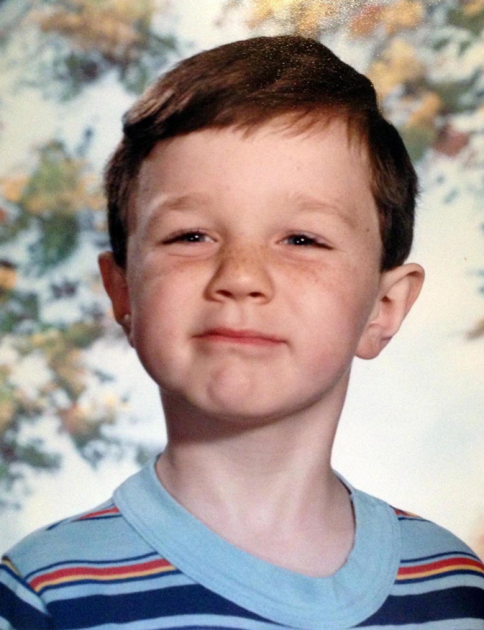 A school portrait of a young boy with freckles wearing a striped shirt