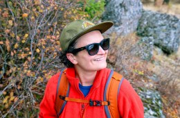 A person wearing an REI Co-op hat, orange fleece jacket and Ray-Ban sunglasses smiles off into the distance.