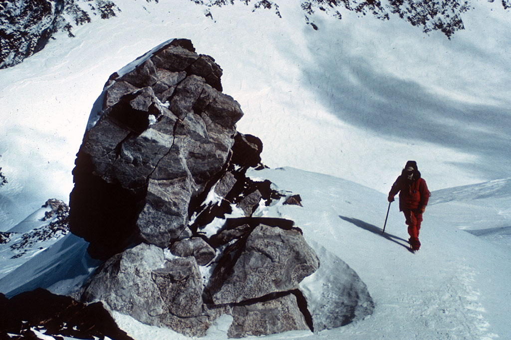 A figure of a mountaineer near a rocky outcropping on a snow-covered mountain.