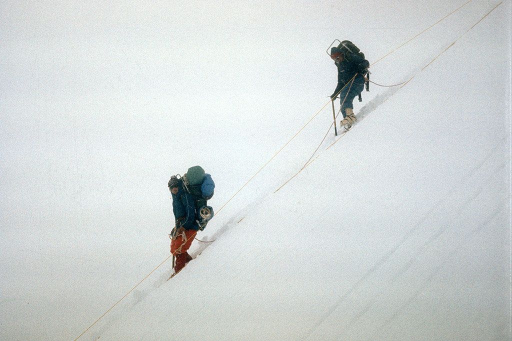 Two mountaineers are seen descending a steep snow-covered mountain.