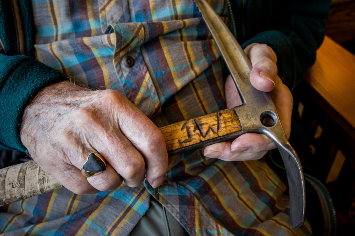A close-up shot of mountaineering legend Jim Whittaker holding a wood ice axe with the initials J.W. carved into the shaft