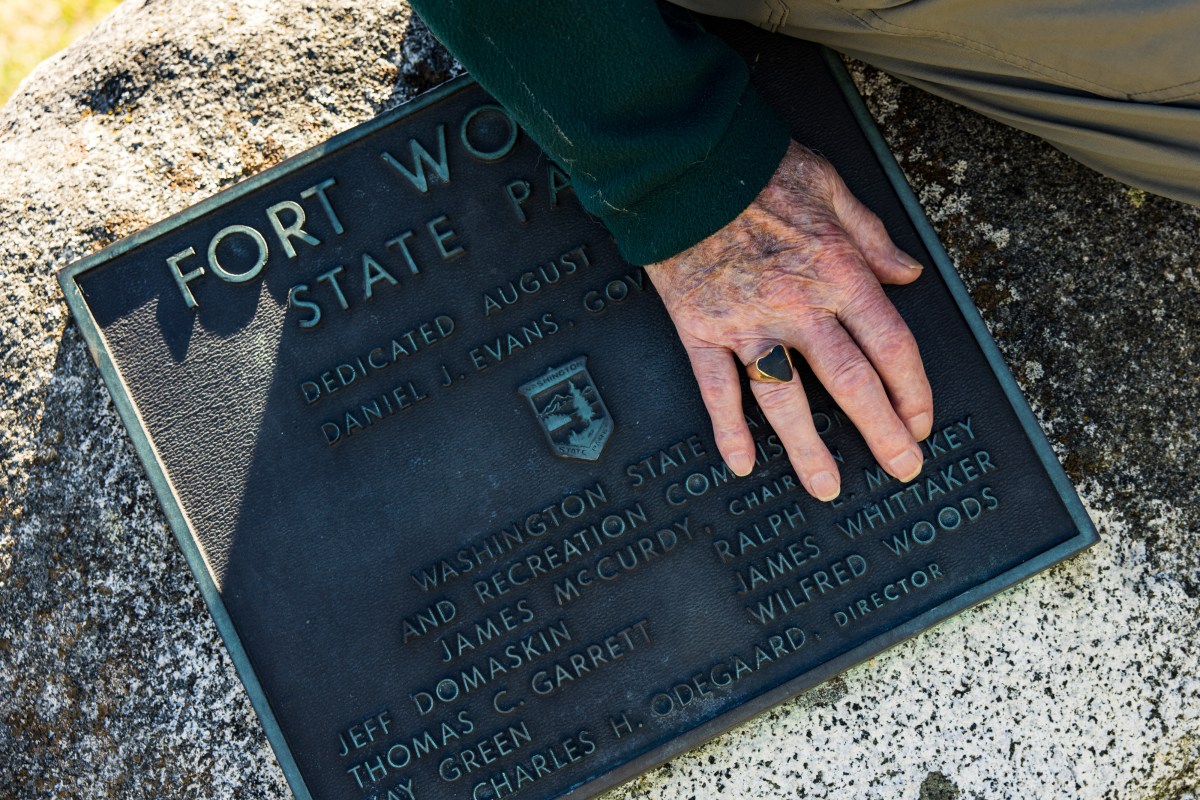 Jim Whittaker places his hand next to a plaque that bears his name. He wears a ring that includes a black stone he took from Everest.